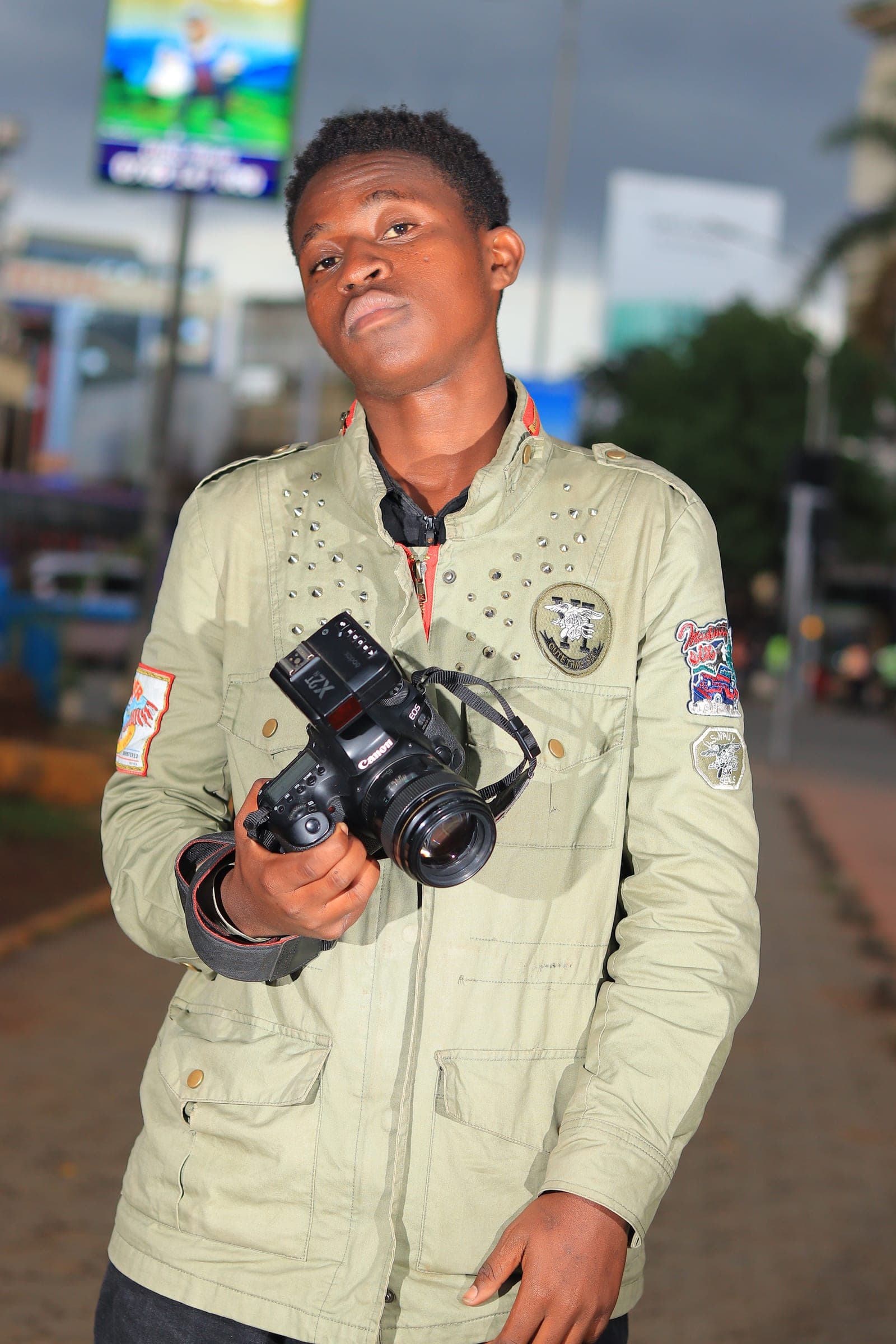 Photographer in an olive jacket holding a Canon camera with a flash trigger in the city