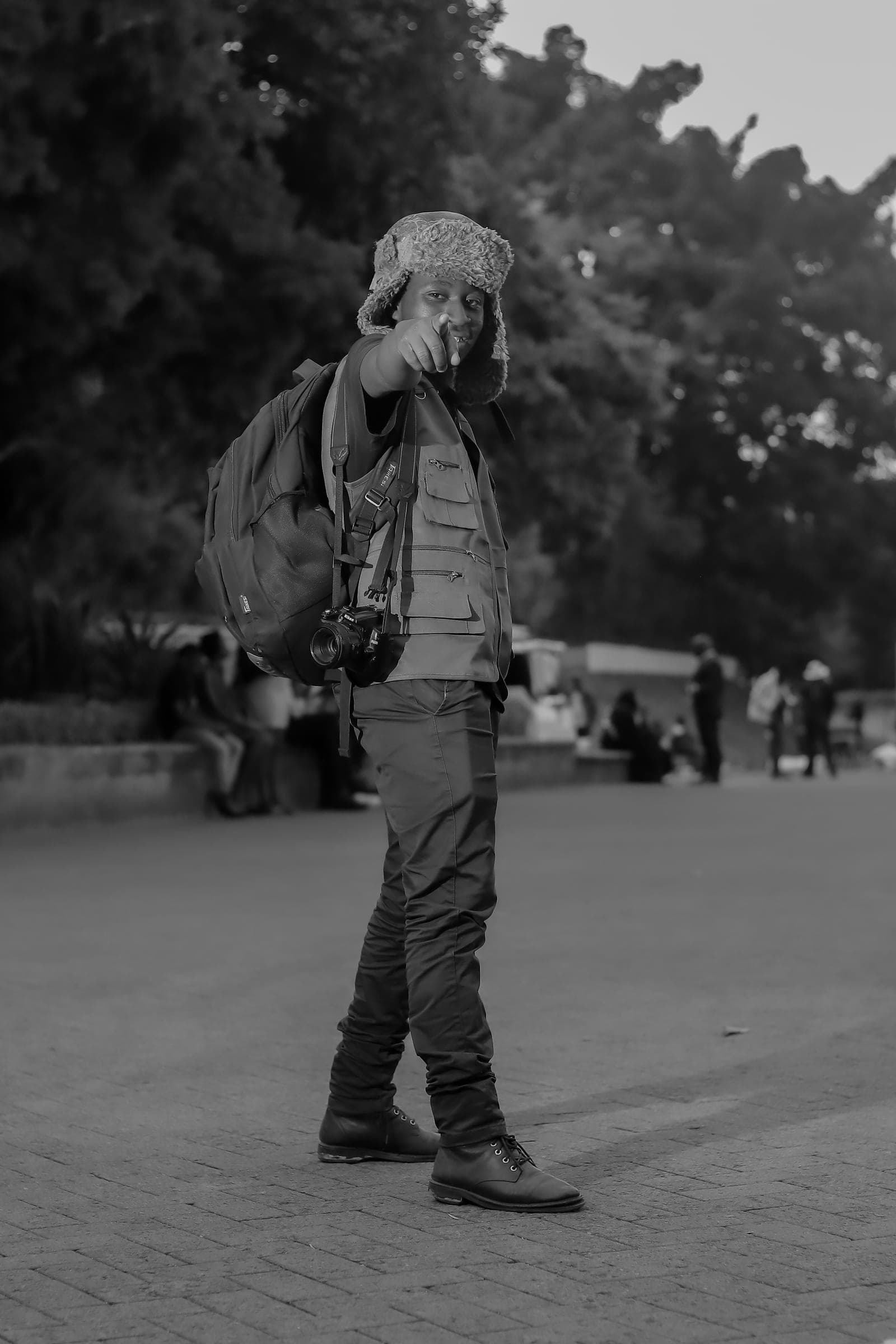 Black and white photo of a Nairobi photographer with a camera and backpack pointing at the viewer