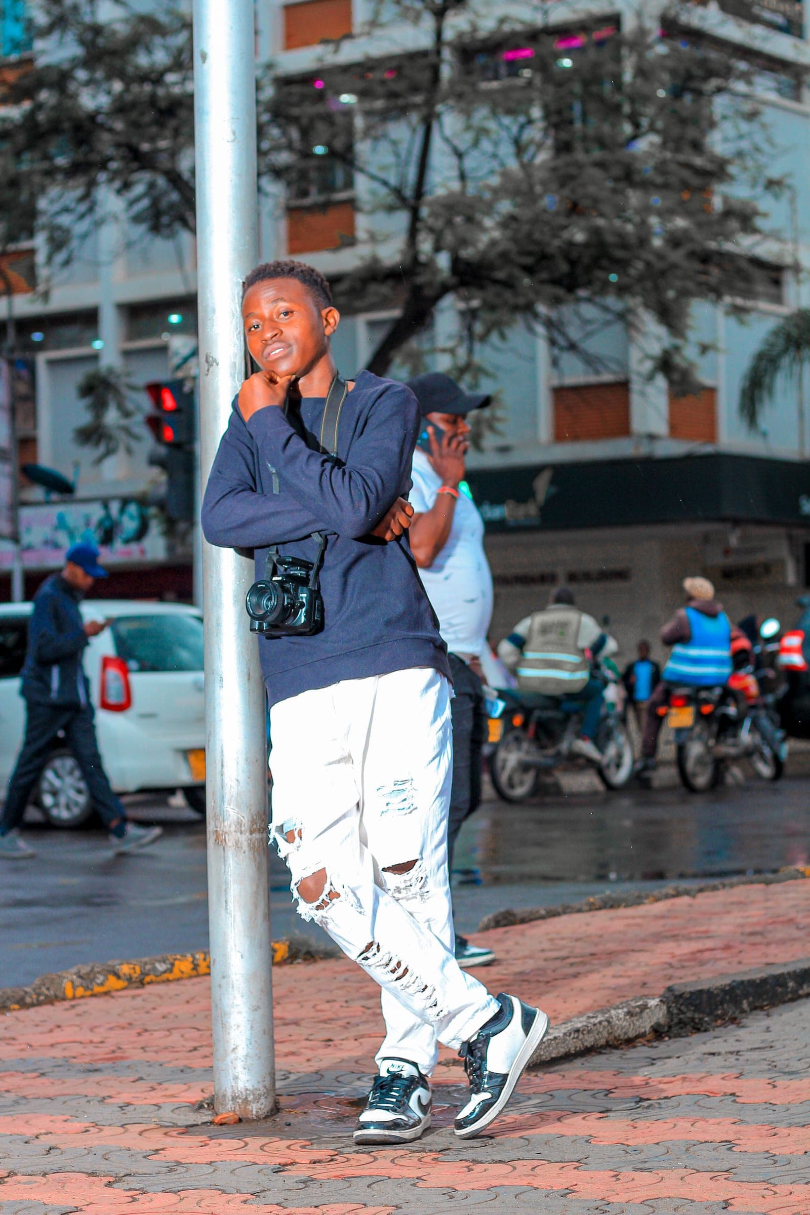 Photographer leaning on a street pole with a camera, boda bodas in the background