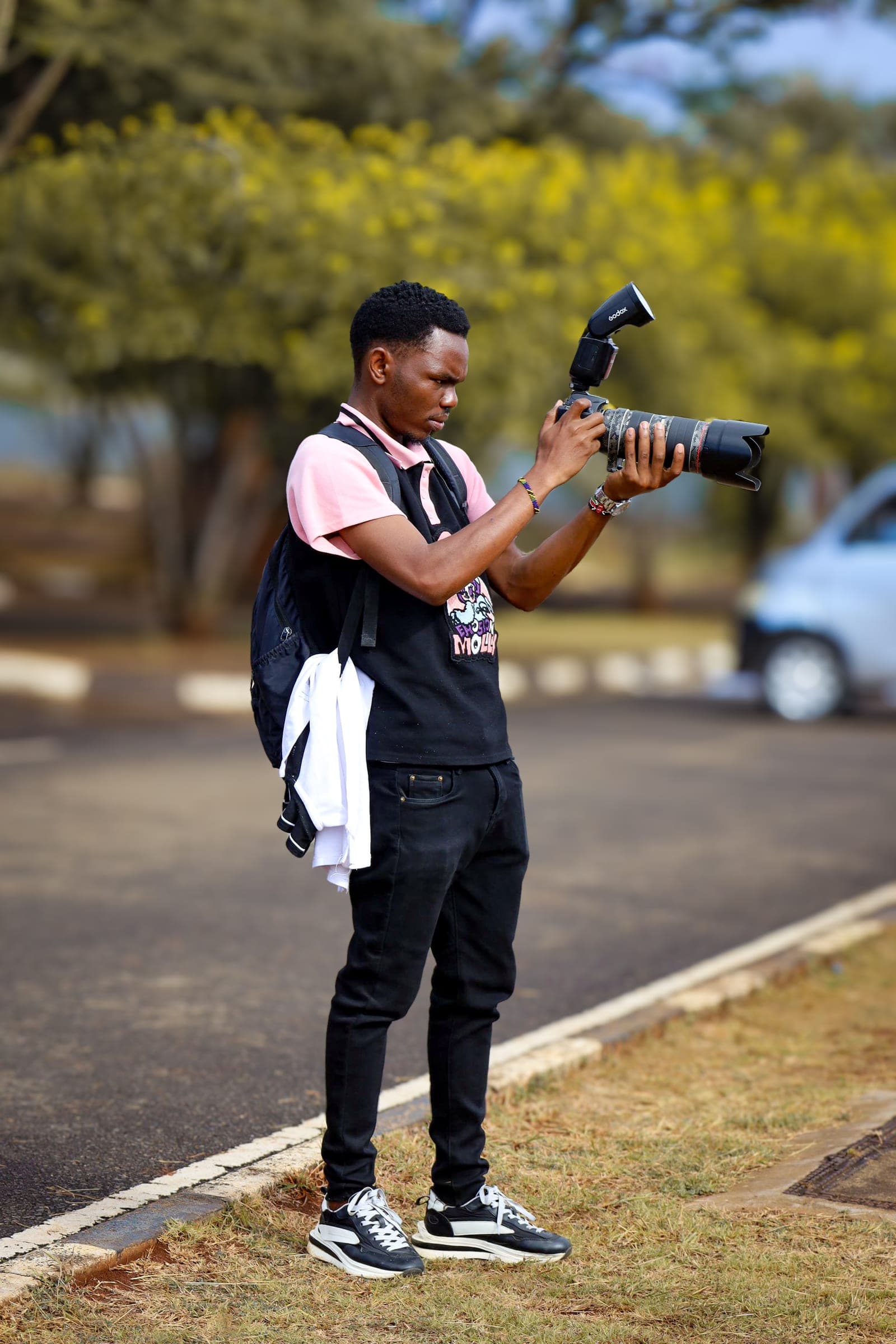 Photographer in a pink polo shooting with a telephoto lens and flash outdoors