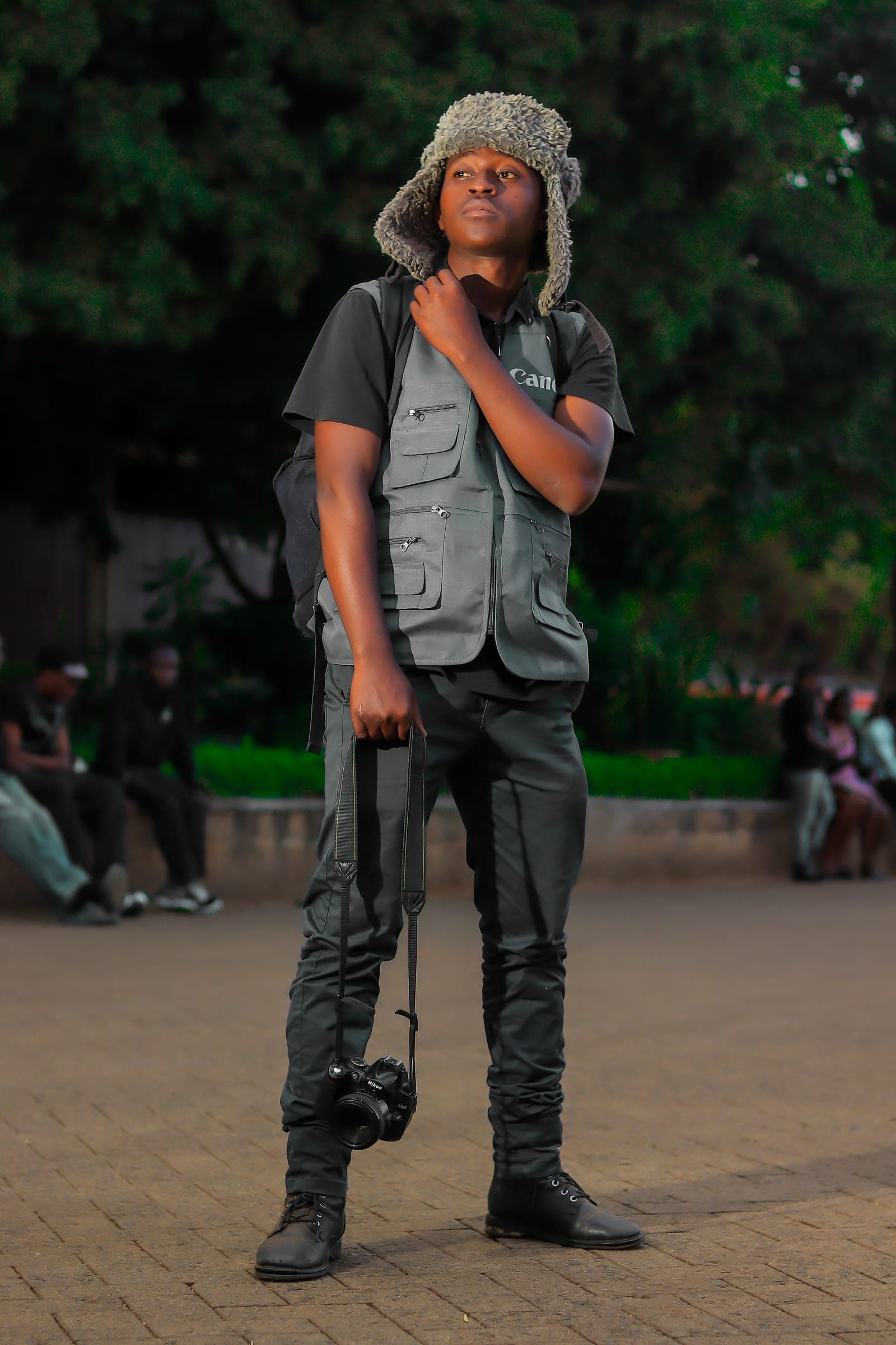 Photographer in a trapper hat and utility vest holding a Nikon camera in a park