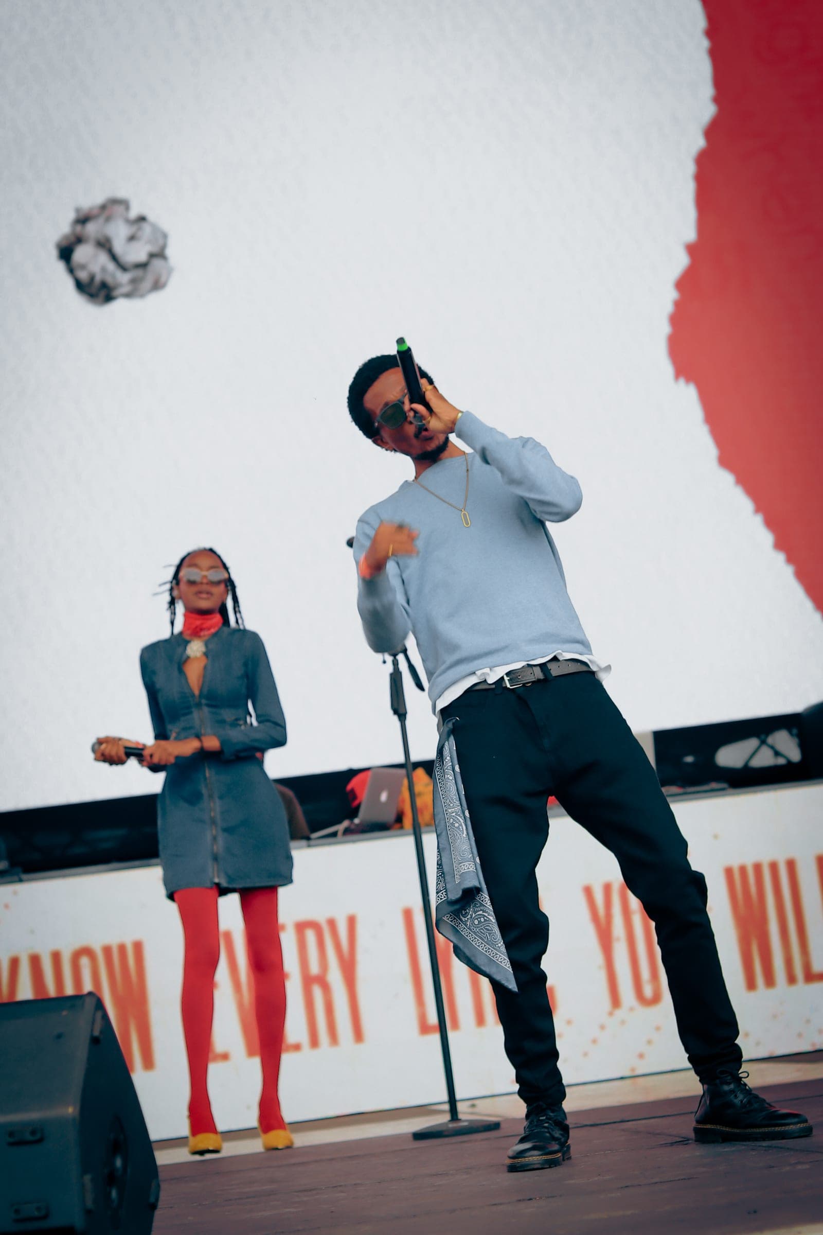 Two performers on stage in front of a red and white backdrop