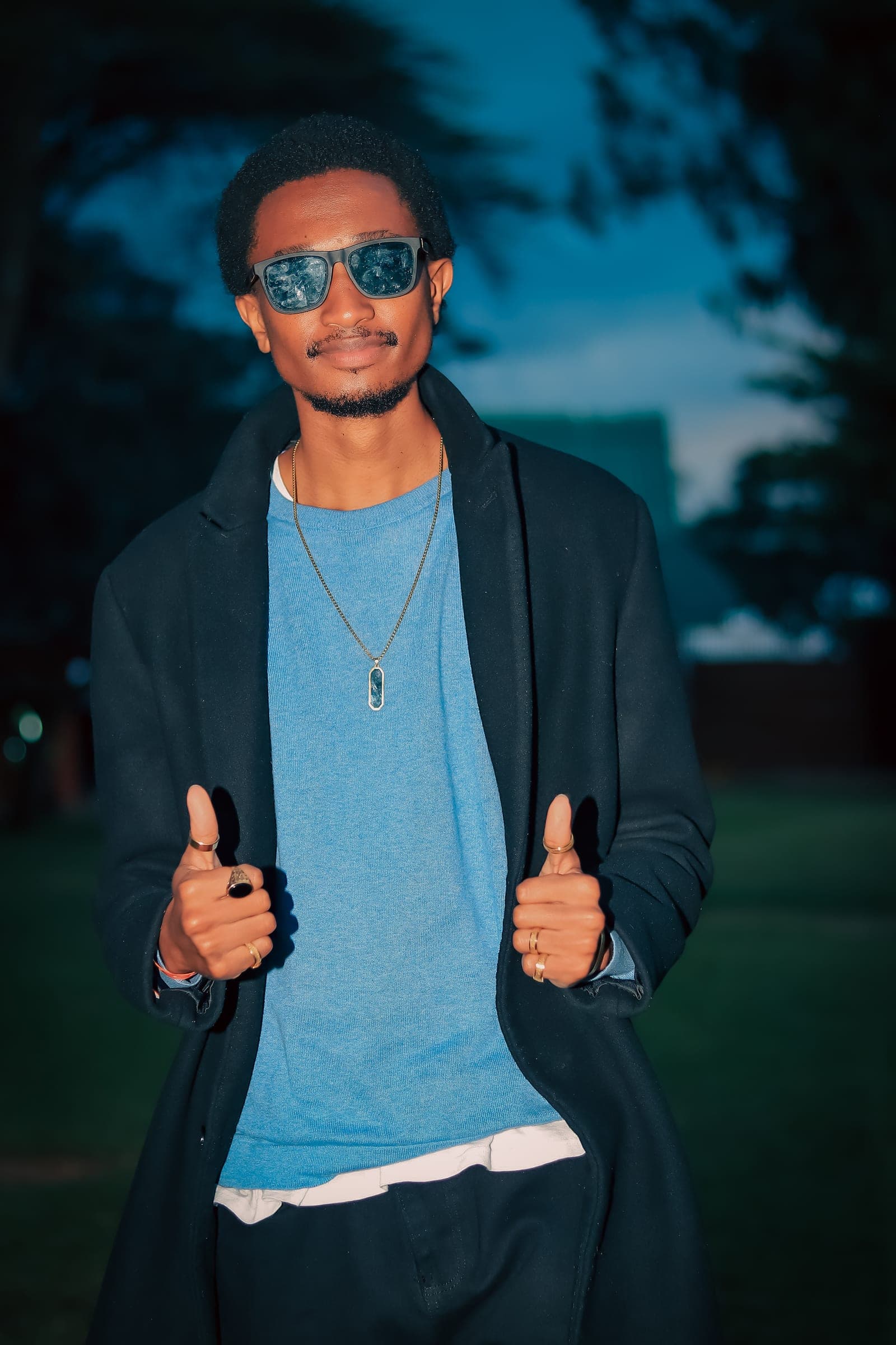 Smiling man in sunglasses giving two thumbs up at dusk