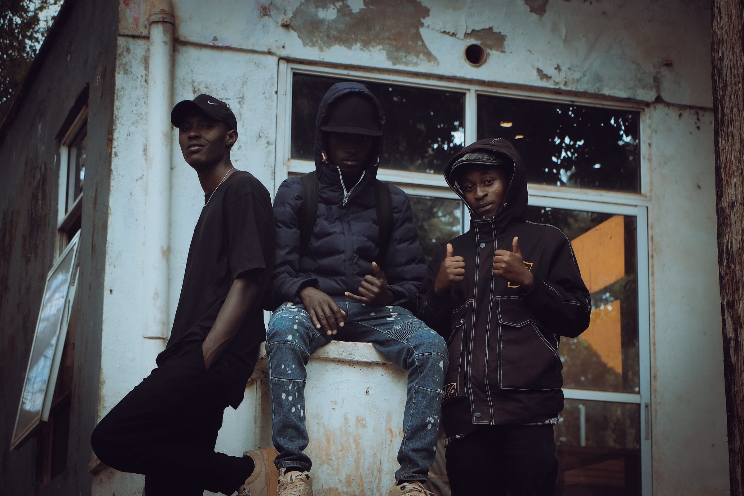 Three friends in dark streetwear posing against a weathered white building